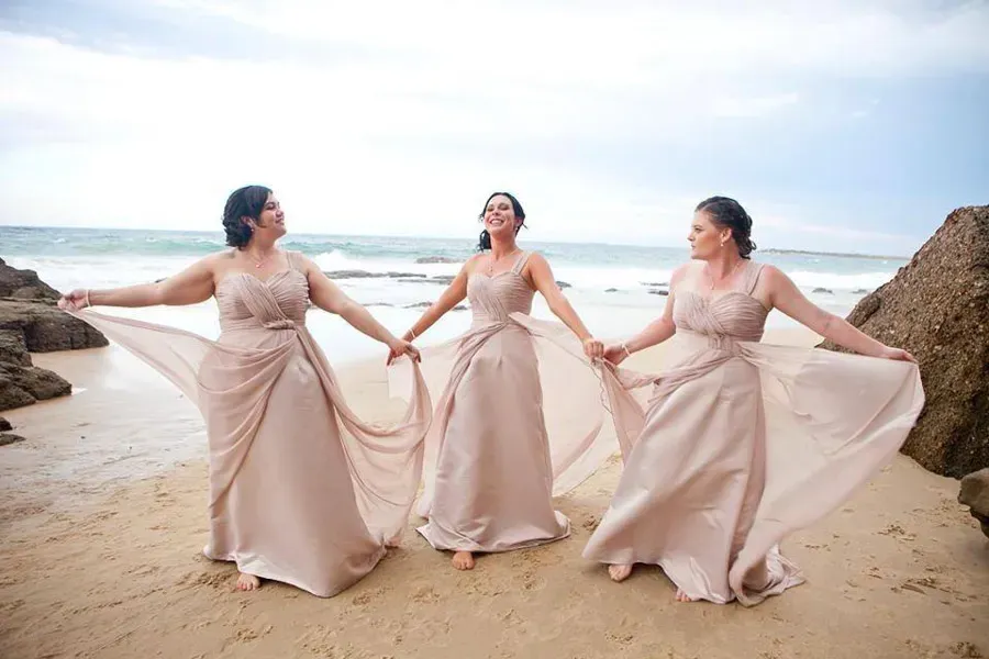 Bridesmaids on the sand in blush gowns, hair styled to hold through a coastal wedding